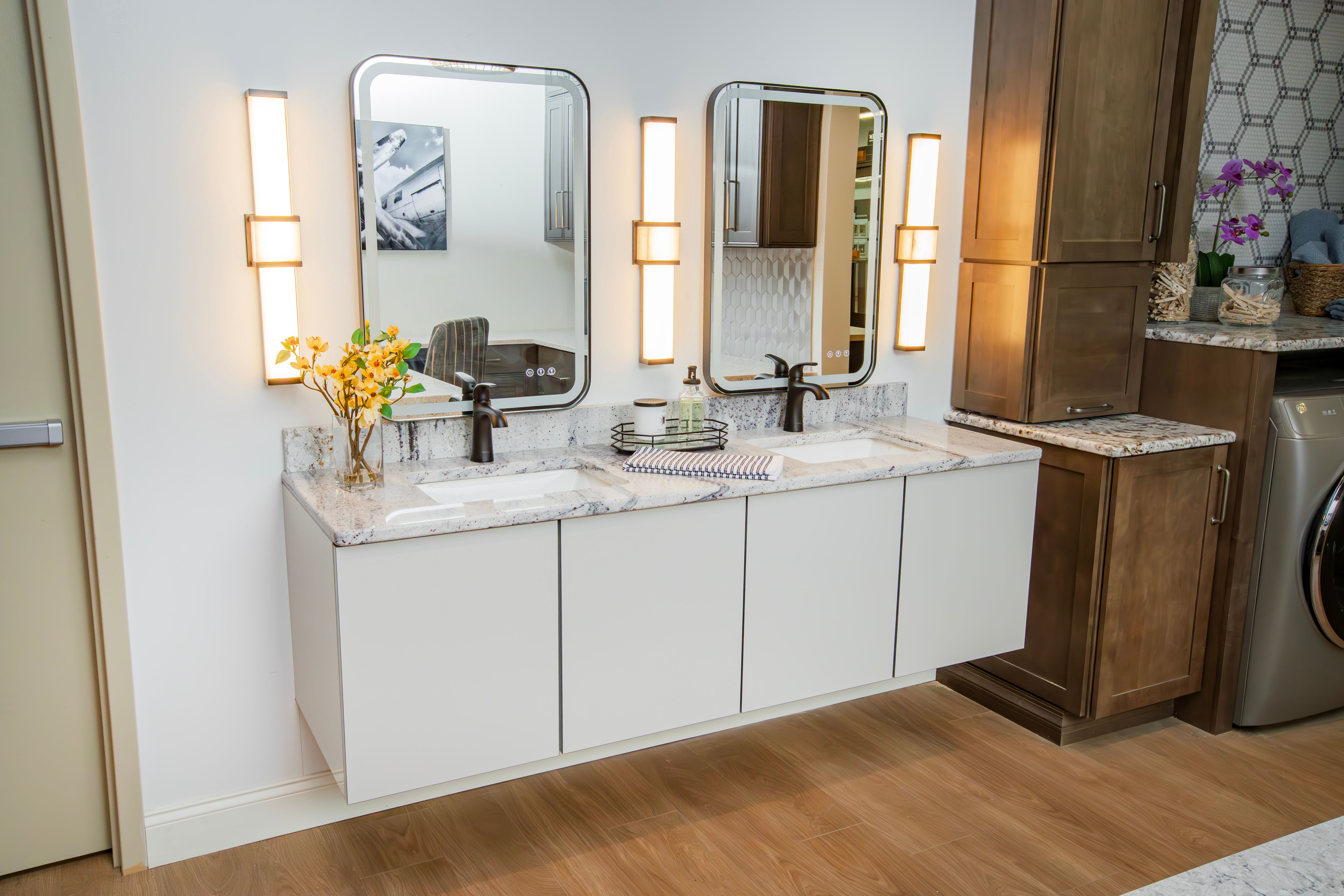 Bathroom display with white floating cabinets and scone lighting surrounding mirrors
